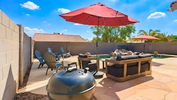 An outdoor patio with a barbecue grill, seating area, and a swimming pool.