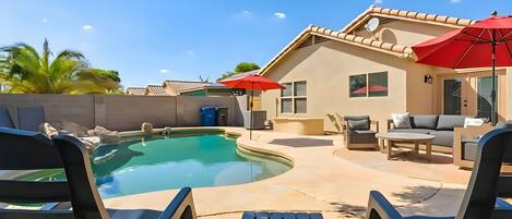 A backyard with a swimming pool, lounge chairs, a red umbrella, and a patio area.