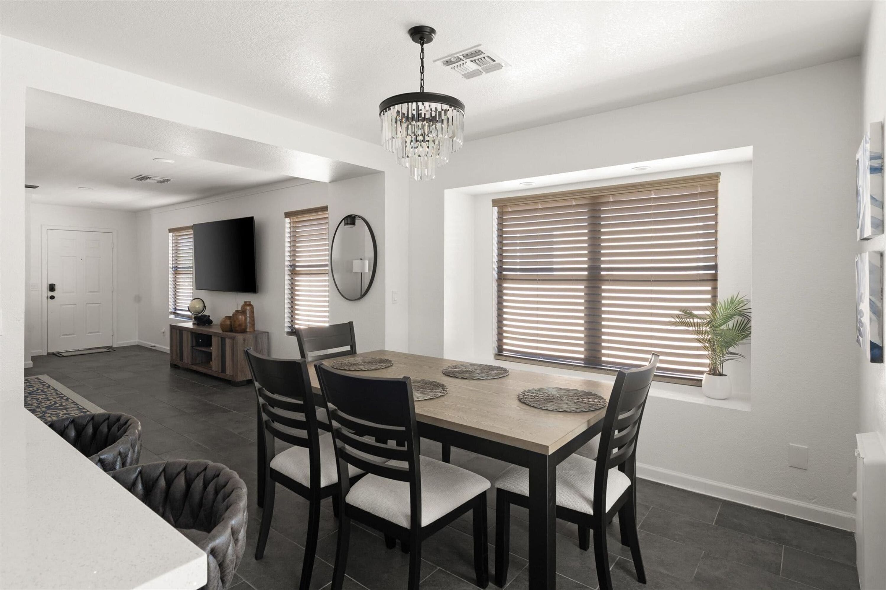A modern dining area with a wooden table, black chairs, and a chandelier.