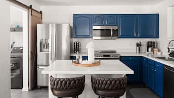 A modern kitchen with blue cabinets, stainless steel appliances, and a central island with two leather stools.