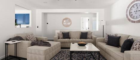 A modern living room with a ceiling fan, a round wall clock, and a patterned rug.