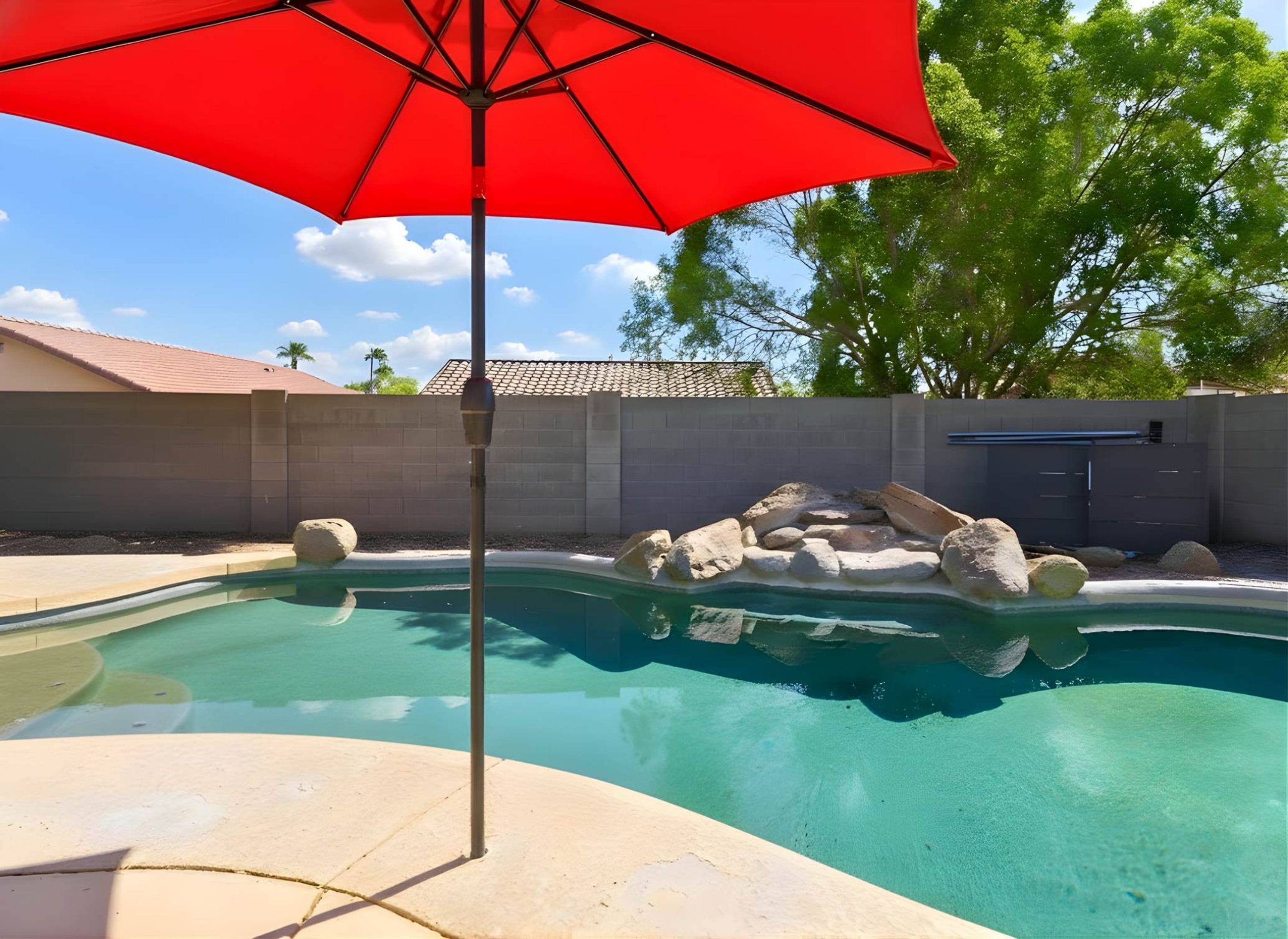 A swimming pool with a red umbrella, surrounded by a concrete wall, and a stone structure in the background.