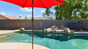 A swimming pool with a red umbrella, surrounded by a concrete wall, and a stone structure in the background.