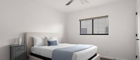 A bedroom with a bed, a nightstand, a ceiling fan, and a window with blinds.