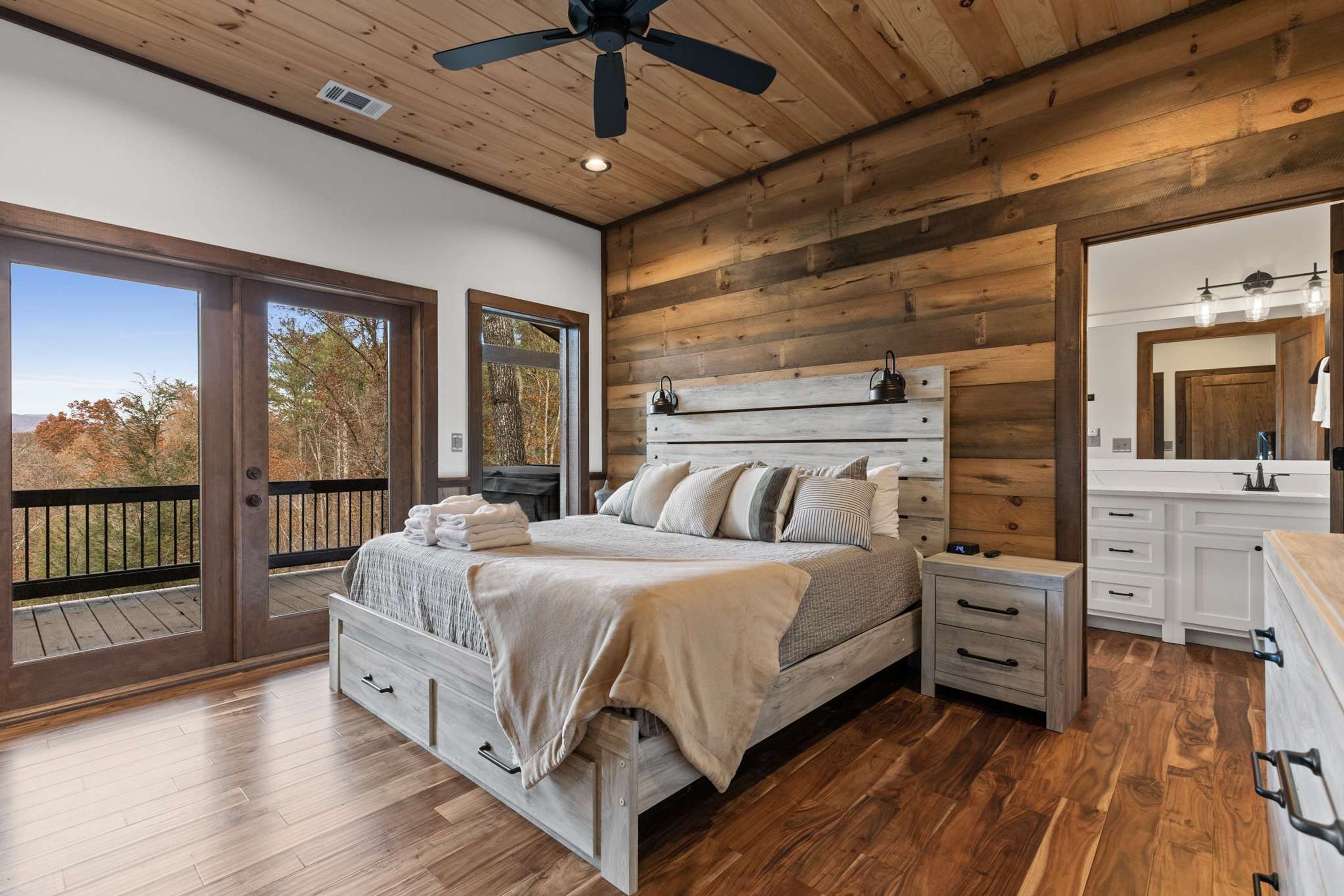 Une chambre avec un plafond en bois, un lit doté d’une tête de lit, des tables de chevet, une commode et une grande fenêtre.