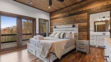 A bedroom with a wooden ceiling, a bed with a headboard, bedside tables, a dresser, and a large window.