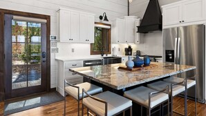 Una cocina moderna con armarios blancos, una isla grande con asientos, un refrigerador de acero inoxidable y una campana extractora negra.