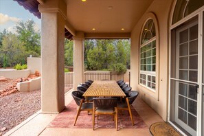 A covered patio with a wooden table and chairs, a large arched window, and a door with glass panels. - NEW Heated Pool Outdoor Fun Hottub Games More (Sedona)