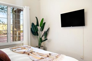A bedroom with a bed, a television mounted on the wall, a window with curtains, and a plant. - NEW Heated Pool Outdoor Fun Hottub Games More (Sedona)