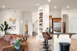 A modern kitchen with a bar area, a dining table, and a living room with a sofa and plants. - NEW Heated Pool Outdoor Fun Hottub Games More (Sedona)