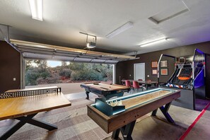 A pool table with a wooden table and a pool cue rack, a ping pong table, and a basketball hoop in a room with a view of a desert landscape. - NEW Heated Pool Outdoor Fun Hottub Games More (Sedona)