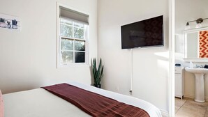 A hotel room with a bed, a television mounted on the wall, a window with blinds, a potted plant, and a bathroom with a sink and mirror. - NEW Heated Pool Outdoor Fun Hottub Games More (Sedona)