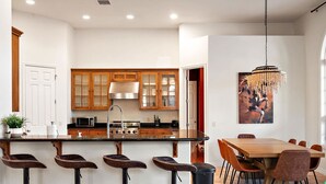A modern kitchen with a central island, bar stools, a dining table with chairs, and a chandelier. - NEW Heated Pool Outdoor Fun Hottub Games More (Sedona)