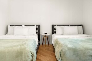 Quarto duplo com duas camas, uma mesa redonda pequena e chão de madeira.