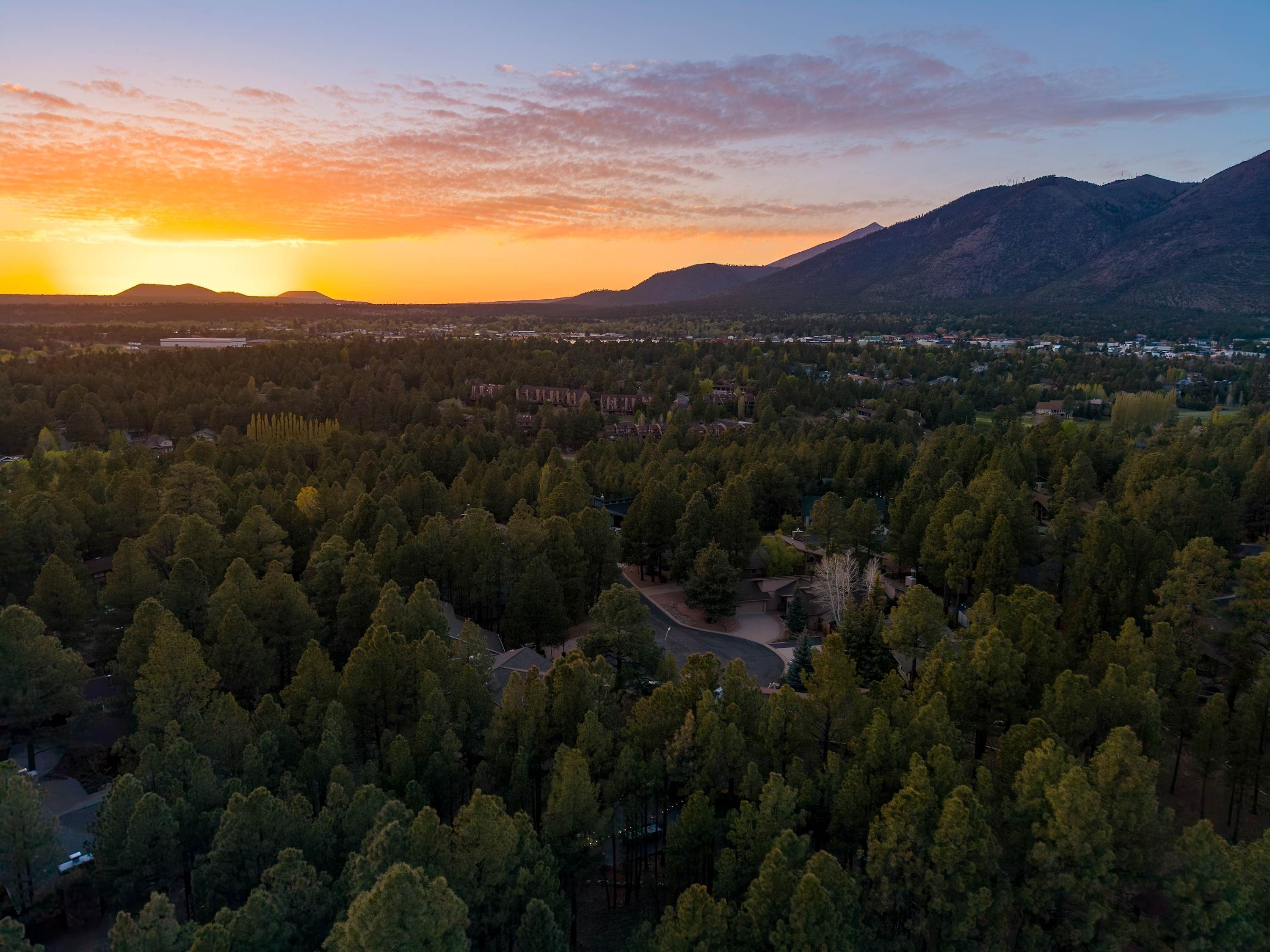 An aerial view of a forested area with a river and a mountain range in the background.