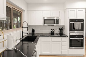 A modern kitchen with white cabinetry, a black countertop, a stainless steel microwave, a kettle, and an oven. - Family-friendly Getaway Hot Tub View EV Chrg (Flagstaff)