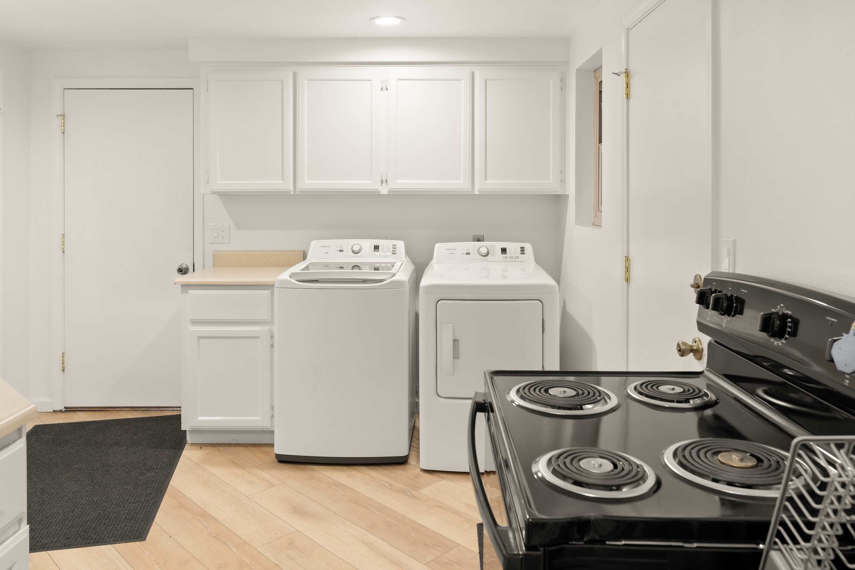 A compact kitchen with white cabinets, a stove, and two washing machines.