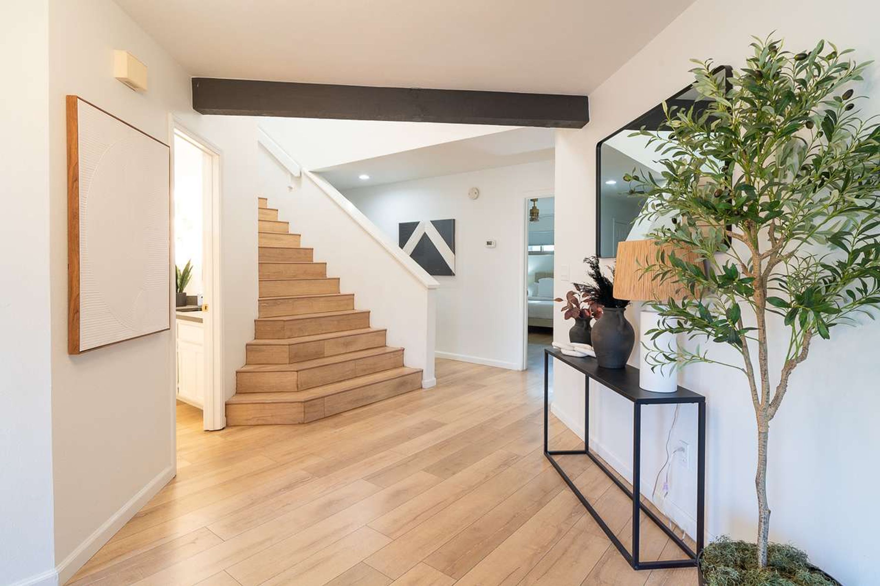 Un interior moderno con una escalera de madera, una consola con una planta y un espejo grande.