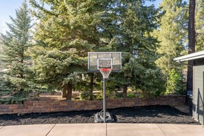 A basketball hoop with a 'LIPSTINE' brand sign, set against a backdrop of evergreen trees and a brick wall. - Family-friendly Getaway Hot Tub View EV Chrg (Flagstaff)