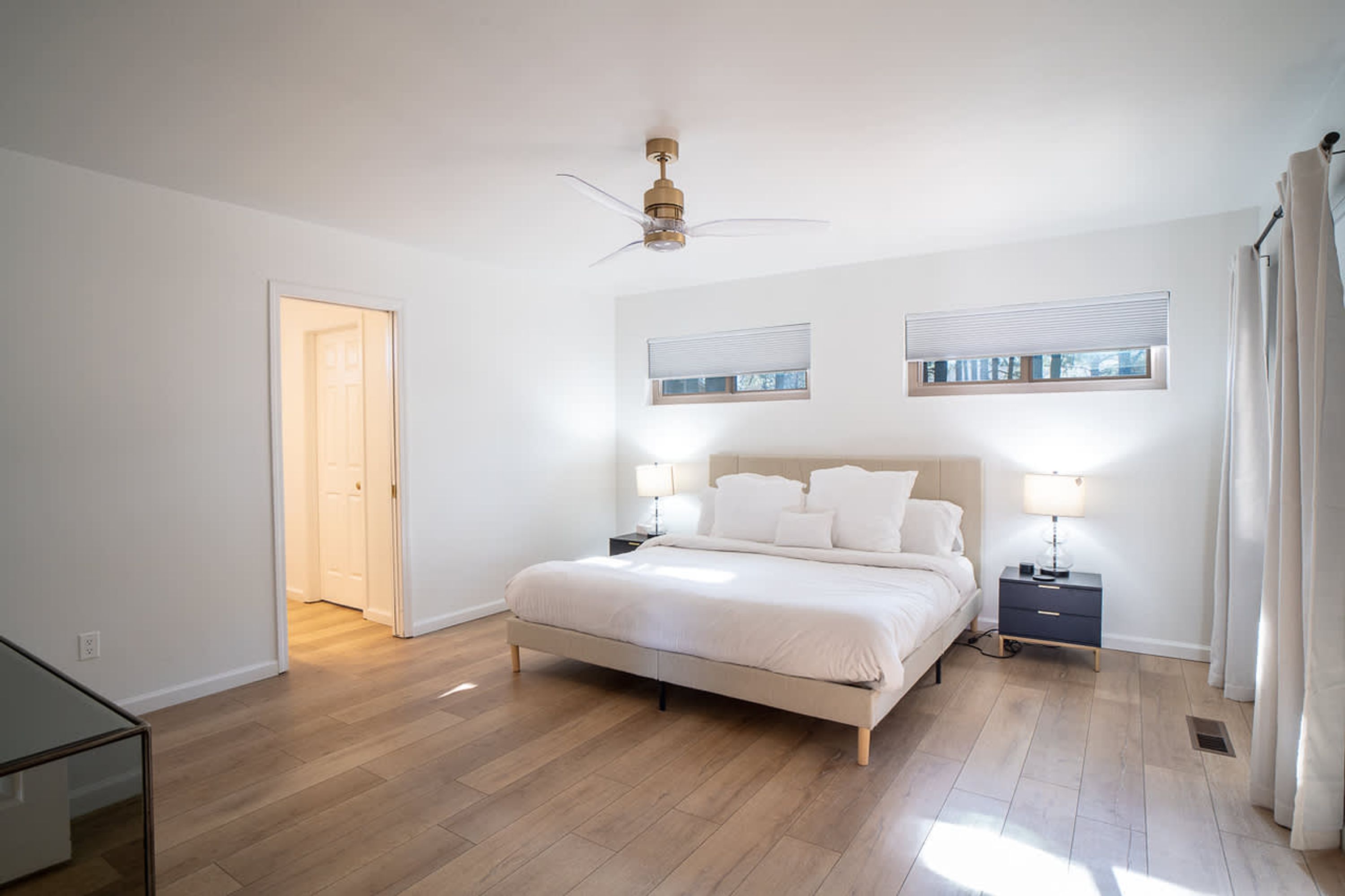 A bedroom with a bed, two bedside tables, a ceiling fan, and two windows with blinds.