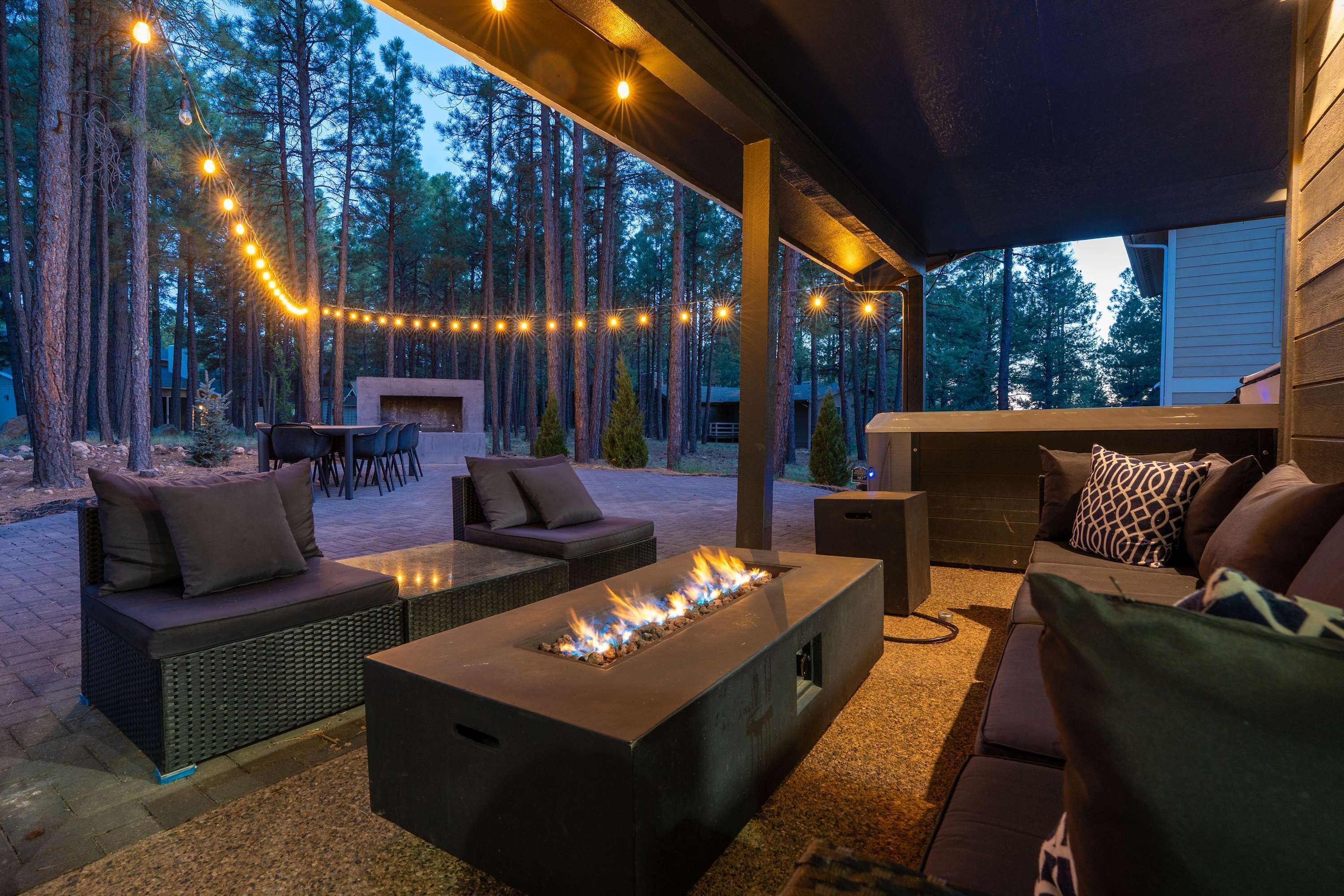 An outdoor patio with a fire feature, seating, and string lights.