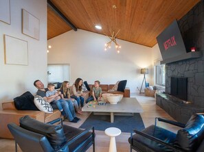 A modern living room with a stone fireplace, a Netflix sign, and a group of people sitting on a couch. - Family-friendly Getaway Hot Tub View EV Chrg (Flagstaff)