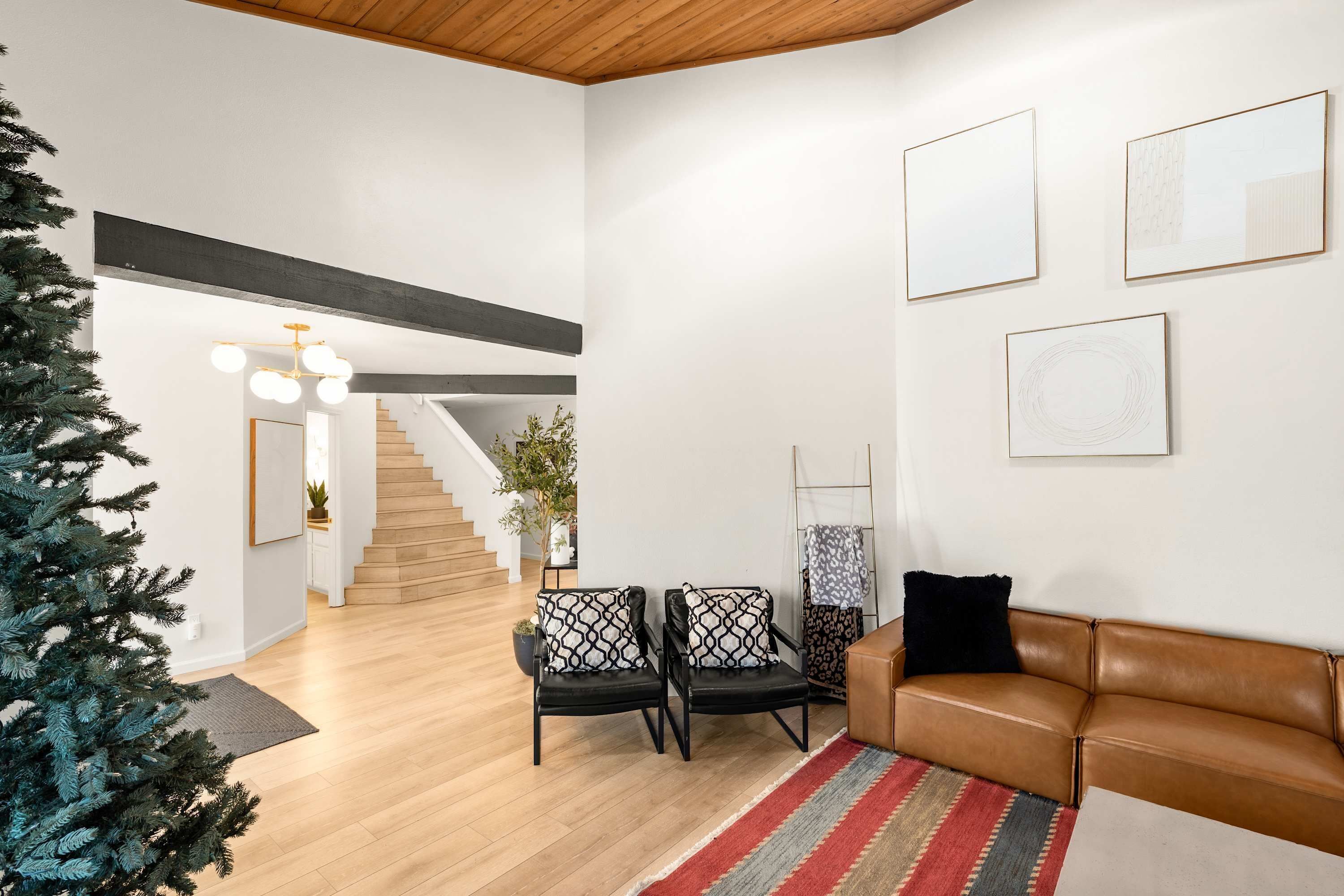A modern living room with a staircase, leather sofa, and artwork on the walls.