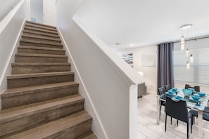 A staircase leading to a dining area with a modern design, a ceiling light fixture, and a window with blinds. - Mins Away From Theme Parks Resort Access Pool (Davenport)