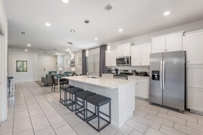 A modern kitchen with white cabinets, stainless steel appliances, and a central island with bar stools. - Mins Away From Theme Parks Resort Access Pool (Davenport)