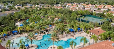 A residential area with a large swimming pool surrounded by palm trees and a tennis court.