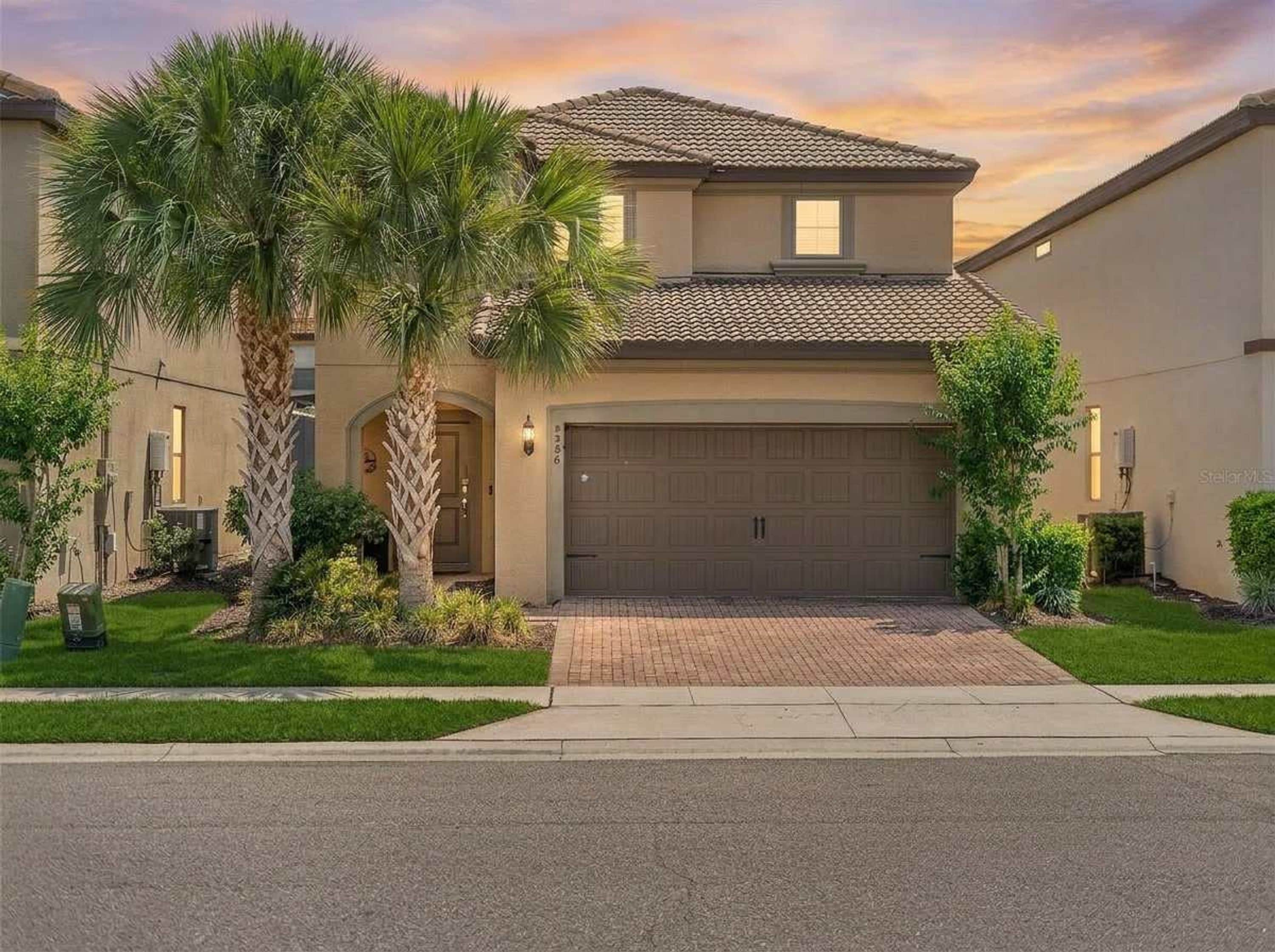 A two-story house with a garage, surrounded by a well-maintained lawn and palm trees.