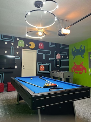 A pool table with a blue felt surface, a red stool, and a foosball table in a room with a wall featuring space-themed decorations. - Mins Away From Theme Parks Resort Access Pool (Davenport)