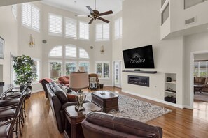 Ein großzügiges Wohnzimmer mit Kamin, Ledersofas, einem Fernseher und Deckenventilator.