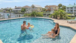 En swimmingpool med ett klart, blått vatten, omgiven av ett poolområde med solstolar och utsikt över bostadshus i bakgrunden.