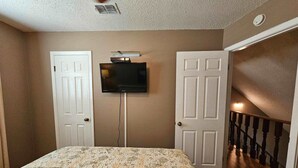 Une chambre à coucher avec un lit, un téléviseur fixé au mur et deux portes.