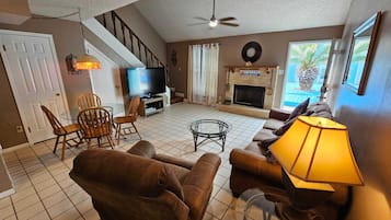 Un salon comprenant un canapé, des fauteuils, un téléviseur, une cheminée et un ventilateur de plafond.