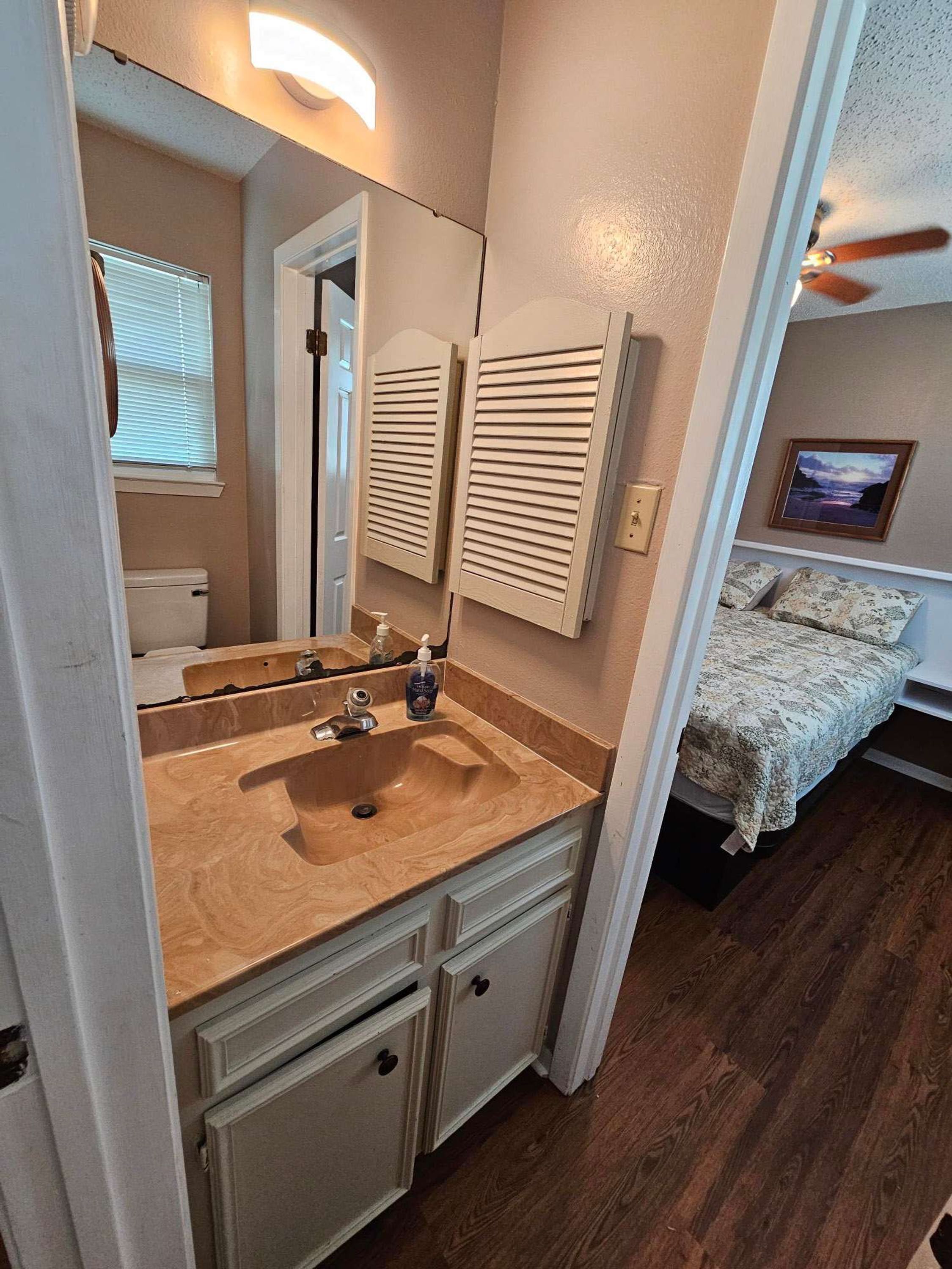 A bathroom with a wooden vanity, a mirror, and a window with blinds.