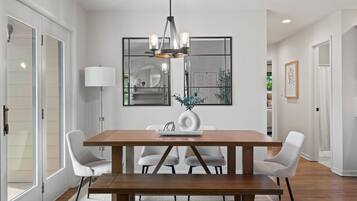 A dining area with a wooden table, white chairs, a hanging light fixture, and a mirror on the wall.
