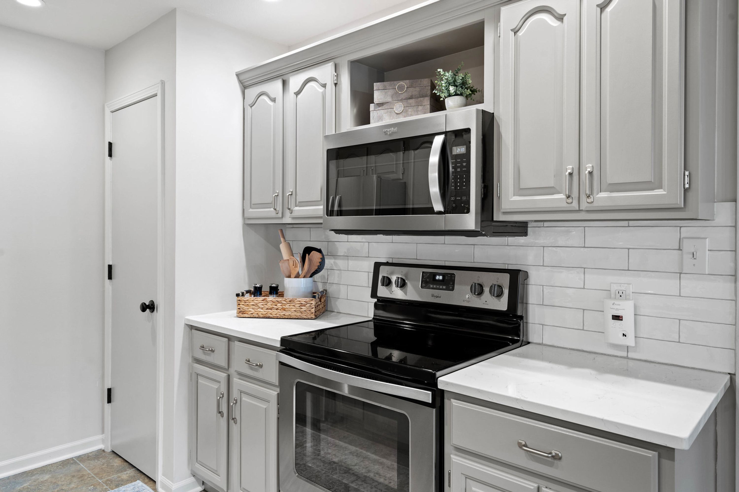 A kitchen with white cabinetry, a black microwave, a stove, and a tiled backsplash.