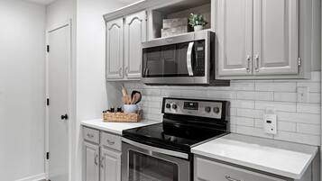 A kitchen with white cabinetry, a black microwave, a stove, and a tiled backsplash.