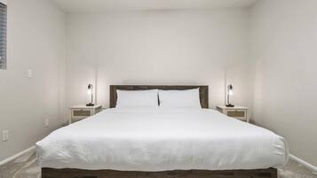 A bedroom with a wooden headboard, a white bedspread, two bedside lamps, and a carpeted floor.