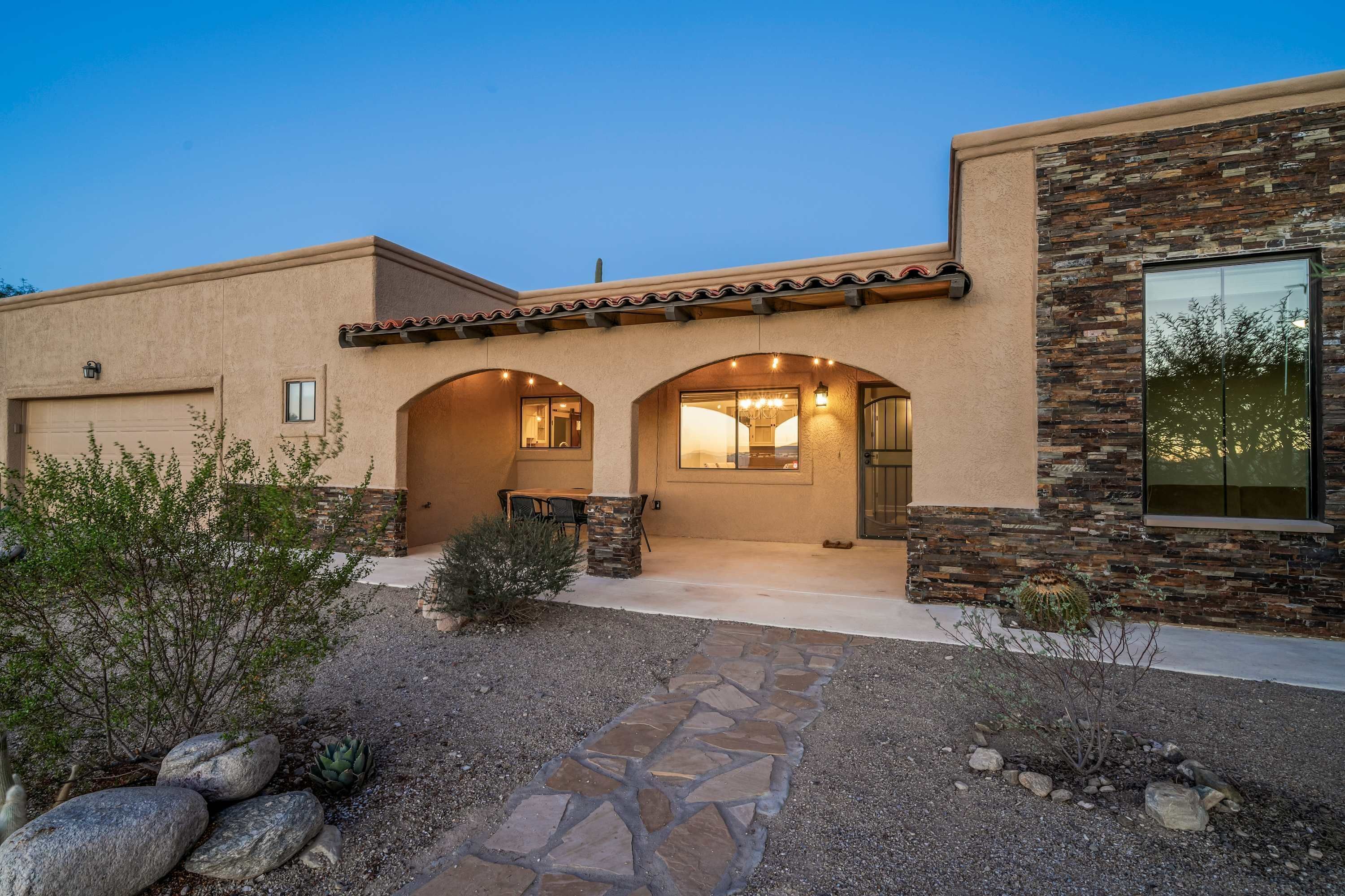 A modern house with a stone facade, a covered patio, and a view of the surrounding landscape.