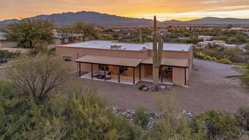 A modern two-story house with a flat roof, a covered patio area, and a large cactus in the foreground.