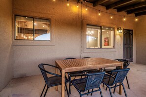 An outdoor dining area with a wooden table and black wicker chairs, string lights, and a textured wall. - 360 Mtn Views Fireplace Patio Bird Watching (Tucson)