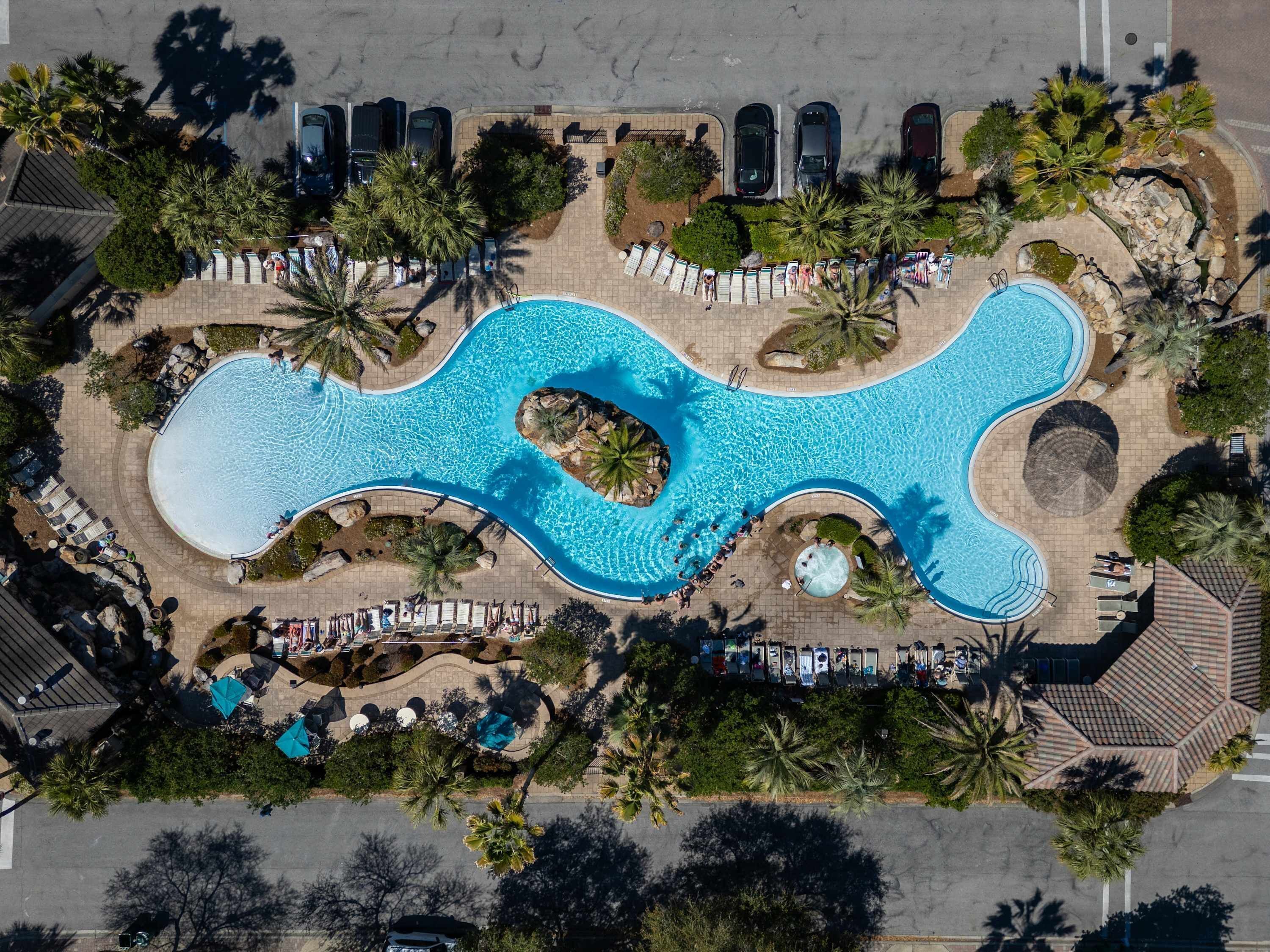 An aerial view of a resort with a large, winding pool surrounded by palm trees and lounge chairs.