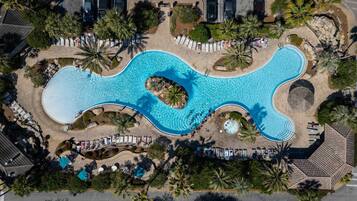 An aerial view of a resort with a large, winding pool surrounded by palm trees and lounge chairs.