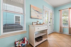 Ein Zimmer mit hellblauer Wand, einer weißen Tür, einem Gemälde, einem Korbwäscheschrank und einem Fenster mit Jalousien.