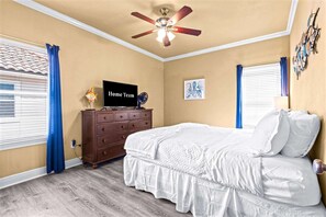 Ein Schlafzimmer mit einem Bett, einem Schminktisch, einem Deckenventilator, einem Fernseher und Kunstwerken an den Wänden.