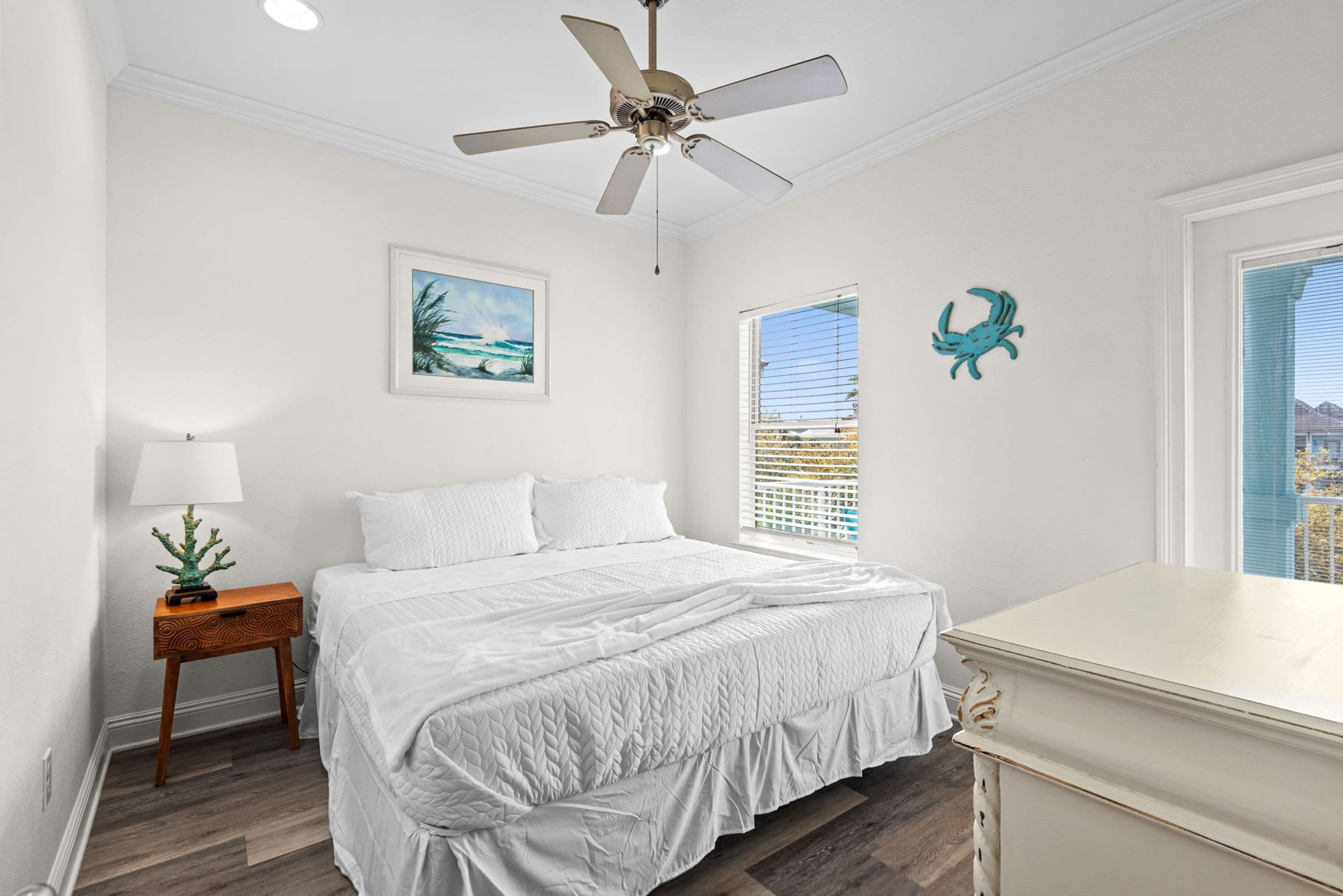 A bedroom with a bed, a nightstand, a ceiling fan, a window with blinds, and a wall-mounted picture.