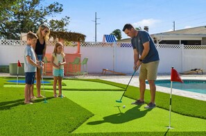 Een zwembadgedeelte met kunstgras, een putting green en een zwembad.
